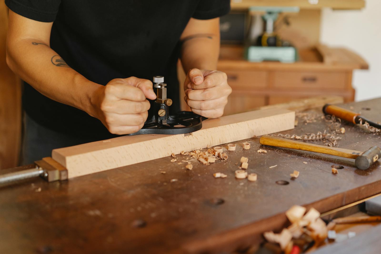 Crop anonymous craftsman working at workbench with manual router plane for making holes in wooden plank in joinery